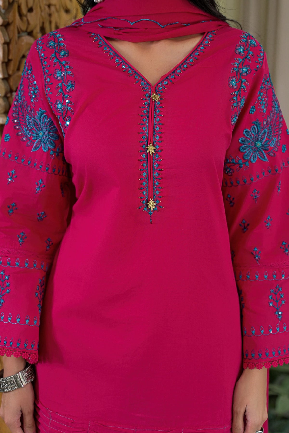 A bright pink kurta with blue floral embroidery and gold star accents down the front placket, worn by a model.