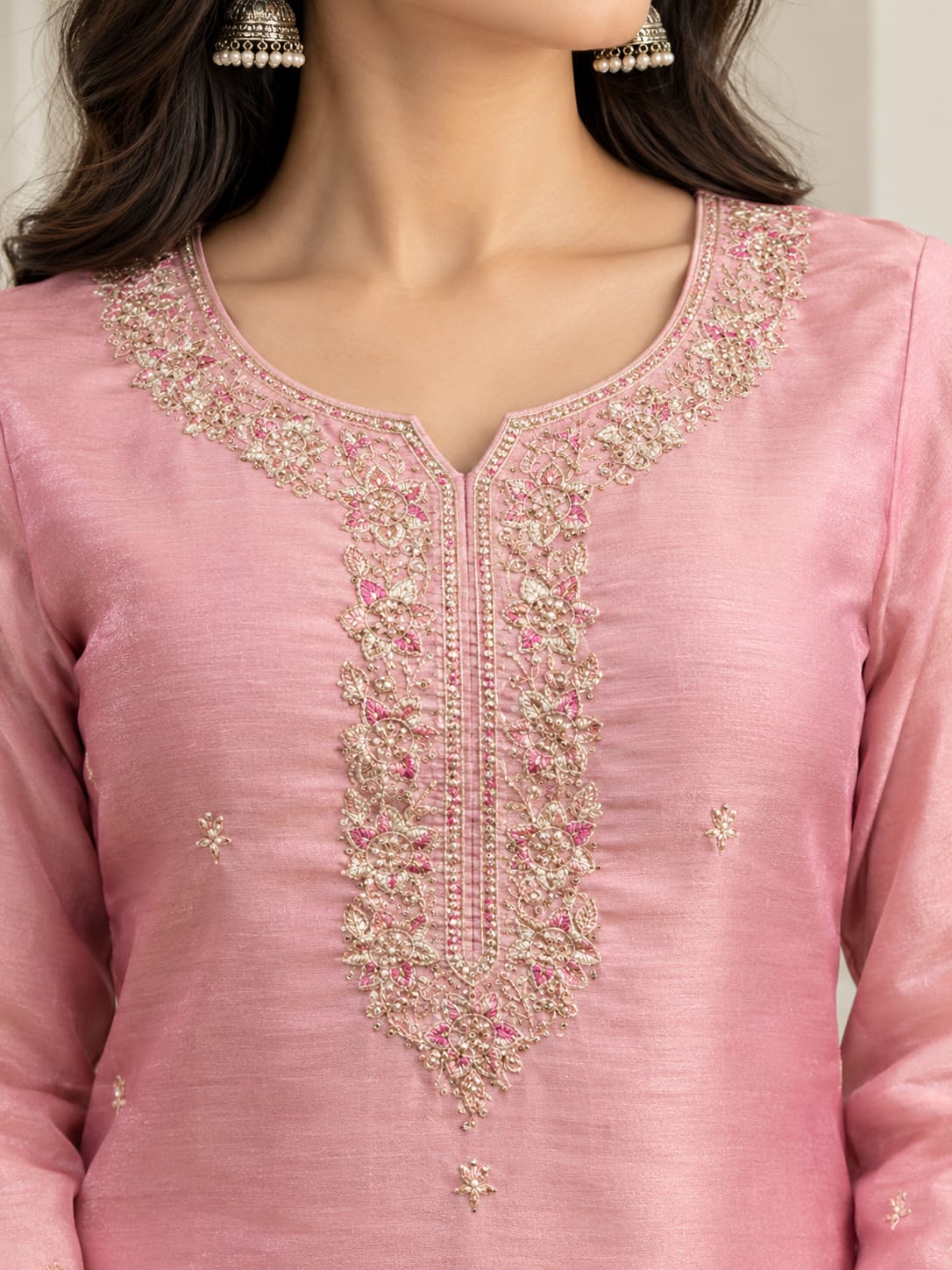 A close-up of a woman wearing a pink kurta with ornate gold and silver embroidery and pink floral details around the neckline.