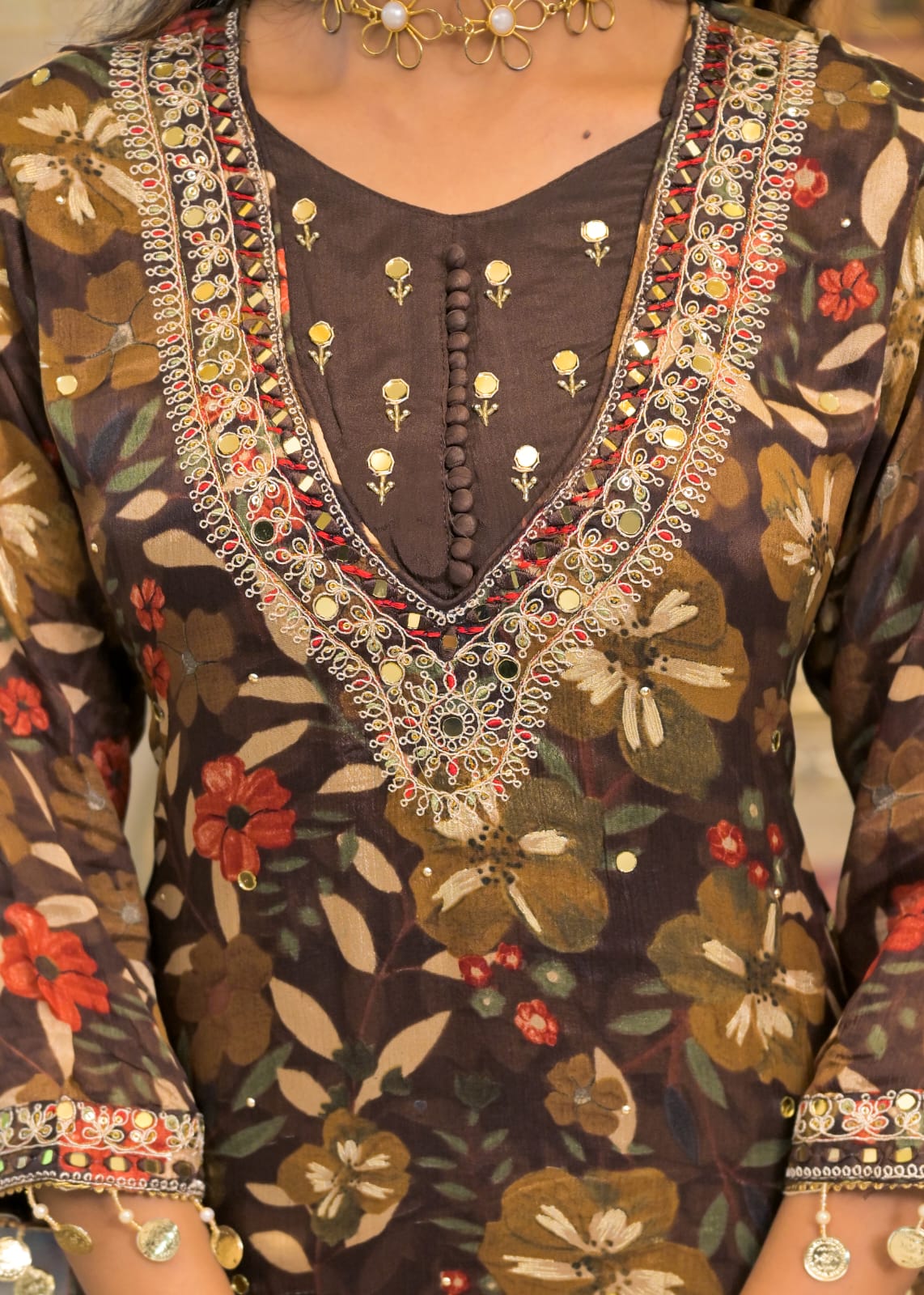 Close-up of a brown floral embroidered kurta with intricate gold, red, and green mirror work around the V-neckline and sleeve cuffs.