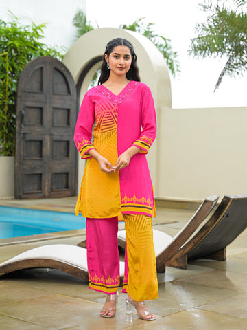 A woman modeling a bright pink and yellow traditional Indian outfit with matching pants, standing outdoors near a pool and lounge chairs.