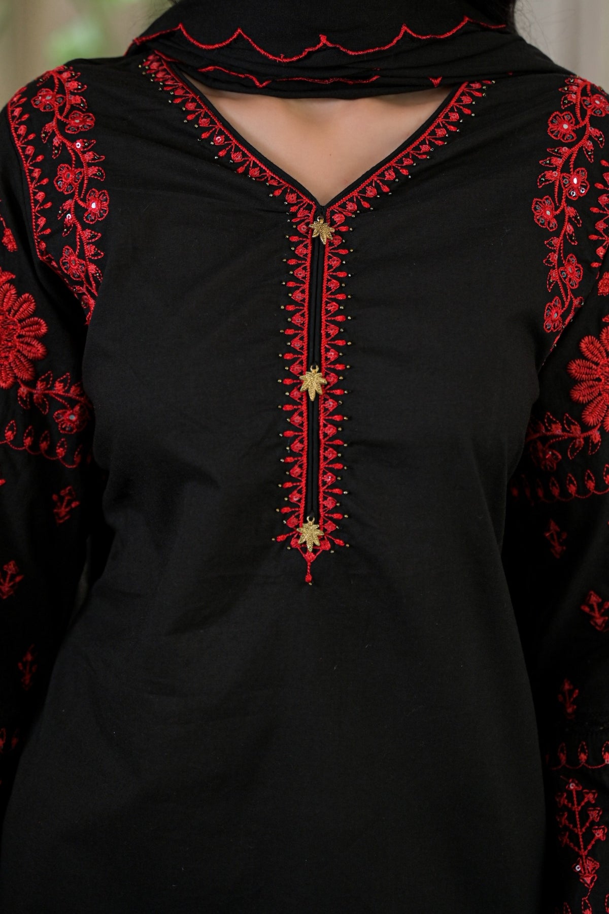 A close-up of a black kurta featuring red floral embroidery on the sleeves and a red embroidered V-neckline with gold decorative accents.