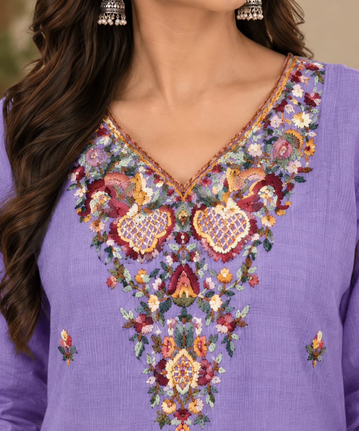 A close-up of a woman wearing a lavender purple kurta with an elaborate, colorful floral and paisley embroidered neckline.