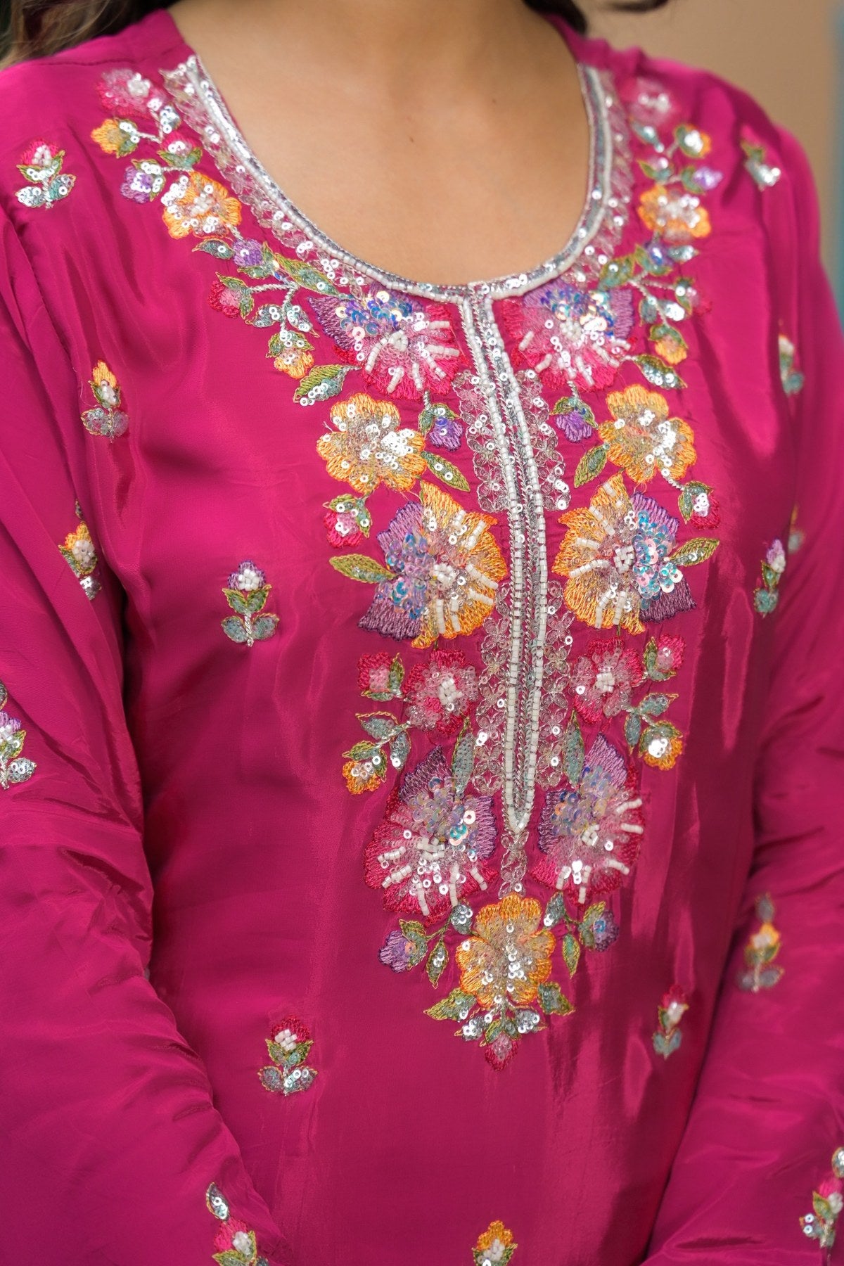 A close-up of a bright magenta pink traditional kurta featuring intricate floral embroidery and sequin embellishments around the neckline and down the center front.