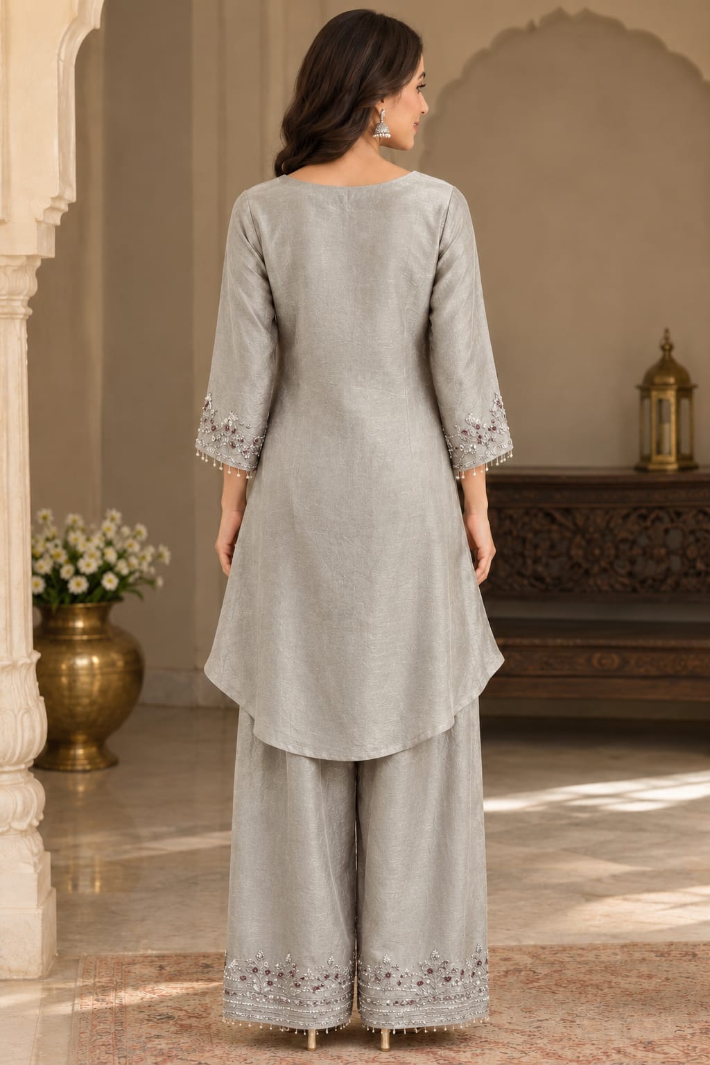 A woman stands with her back to the camera wearing a light gray three-piece traditional outfit with matching wide-leg pants. The set features three-quarter sleeves with delicate lace trim at the cuffs and matching lace detailing along the hems of the pants.