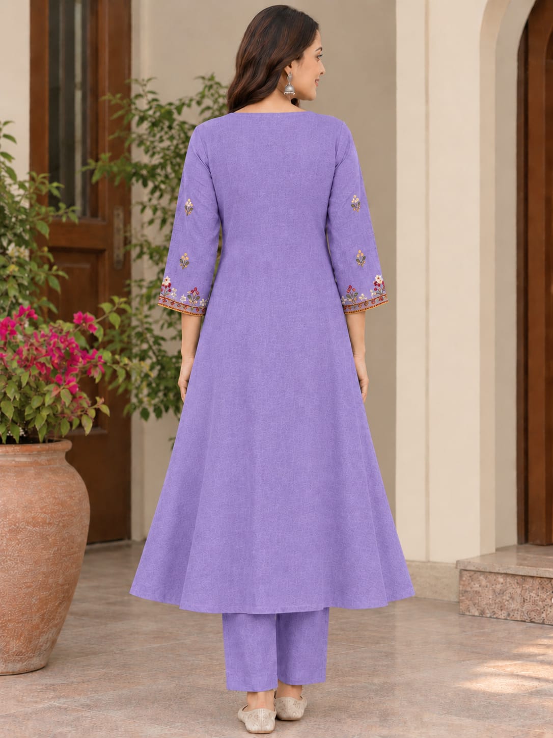 A woman is shown from the back wearing a lavender purple kurta and matching trousers. The kurta features three-quarter sleeves with colorful floral embroidery near the cuffs.
